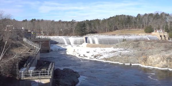 Water flowing over a dam in a river surrounded by trees.