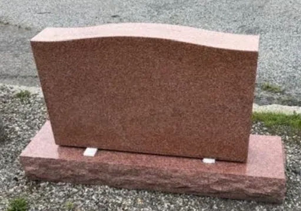 Blank pink granite gravestone on gravel.