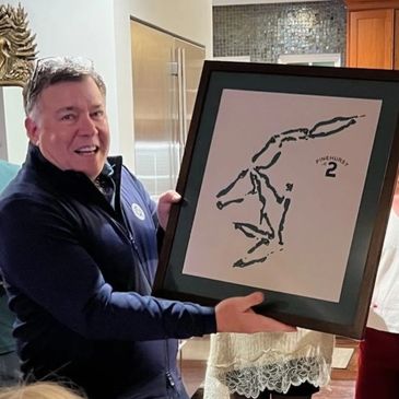 Man proudly holding framed art with others watching in a cozy indoor setting.