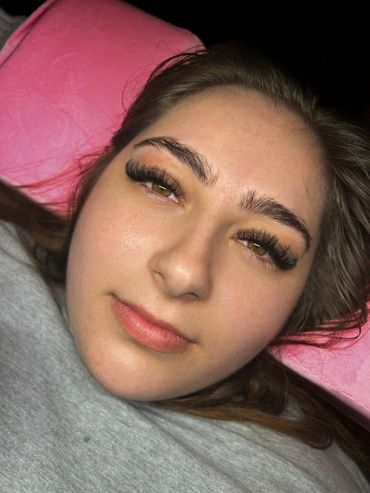 Close-up of a young woman with long eyelashes lying on a pink pillow.