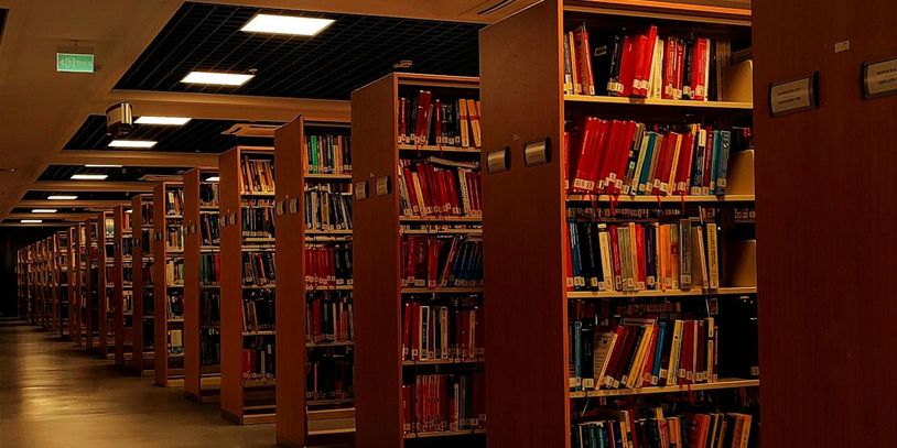 Rows of wooden bookshelves filled with colorful books in a dimly lit library.