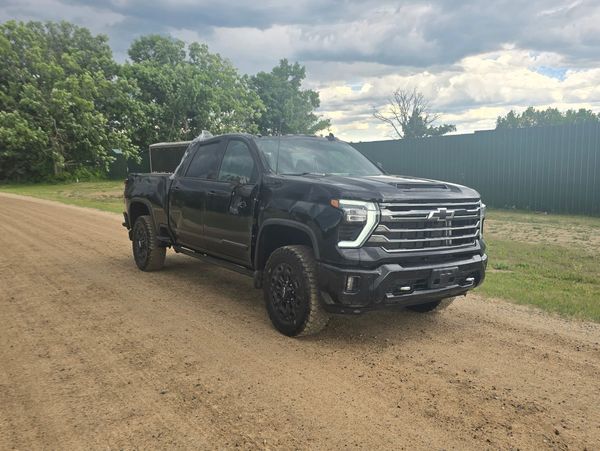 Black Chevrolet pickup truck parked on a dirt road under cloudy sky.