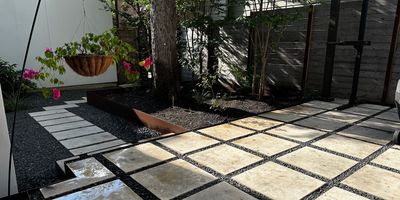 Backyard patio design featuring large square pavers set with dark gravel joints 
