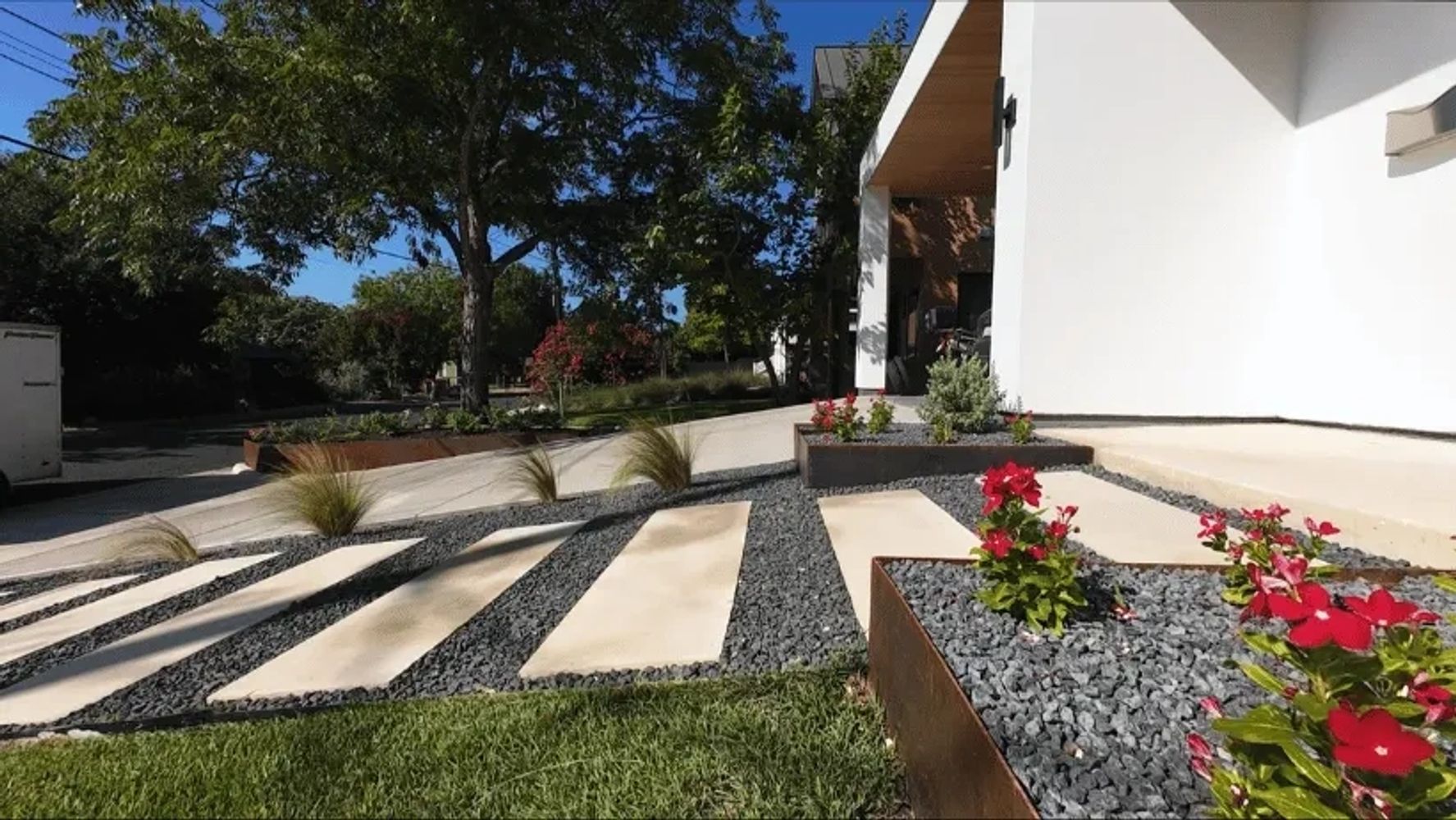 Modern pavers in black gravel lead to a modern white home Steel-edged garden beds with red flowers 