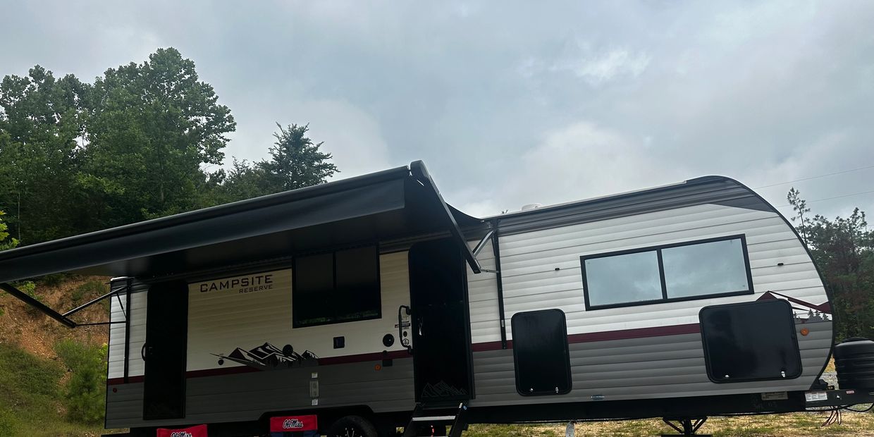 Modern campsite reserve trailer with open awning and chairs outside.