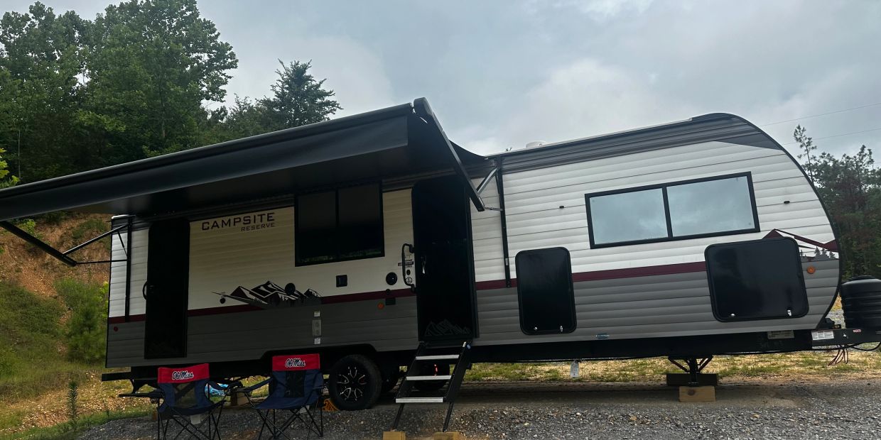Modern campsite reserve trailer with open awning and chairs outside.