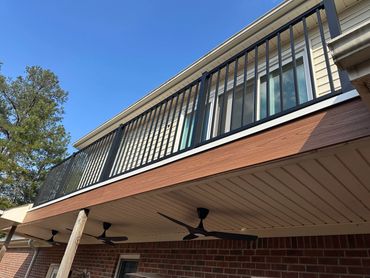 A balcony with black metal railing on a brick house under a clear sky.