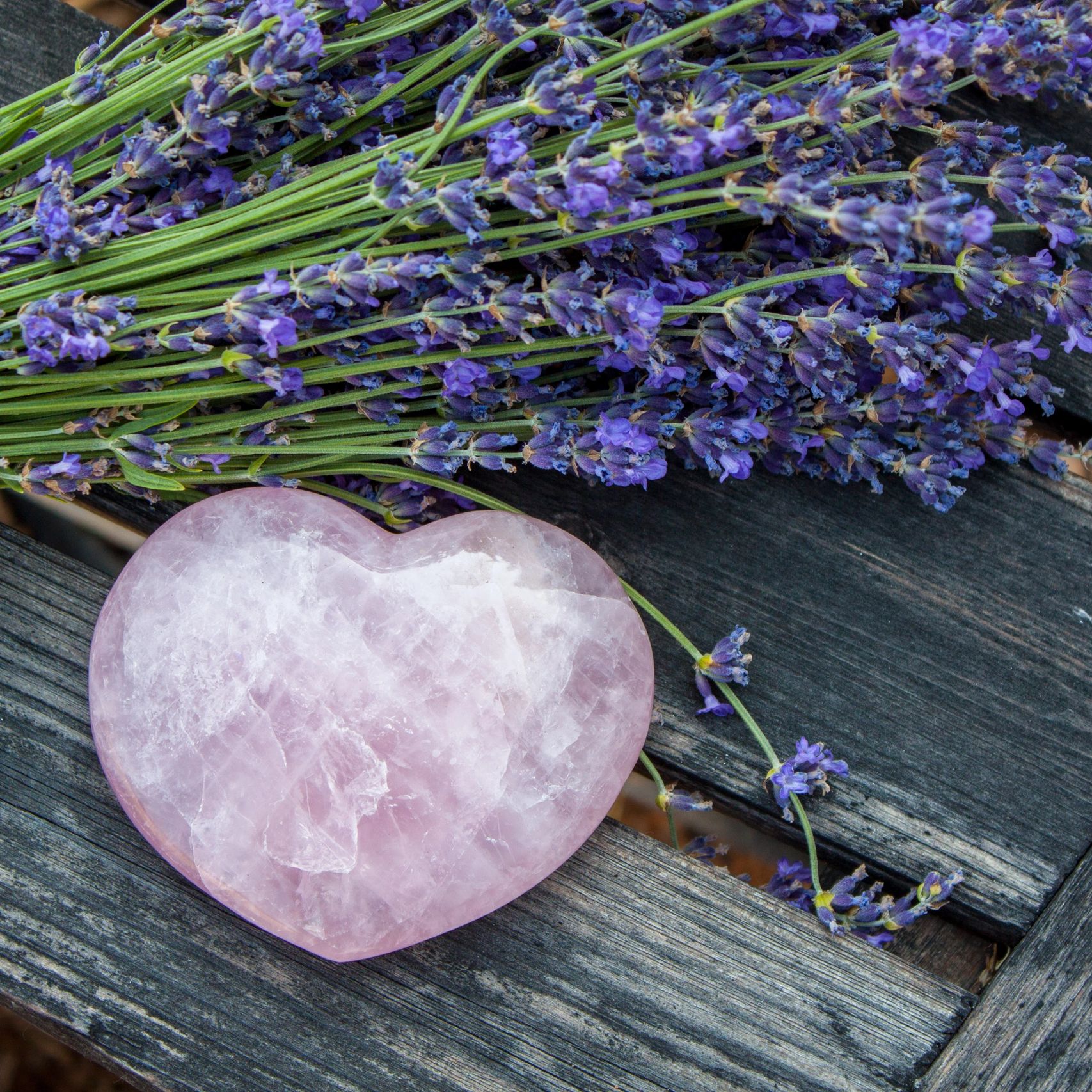 Heart-shaped rose quartz with lavender on rustic wooden surface.