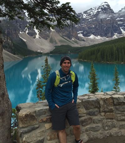Man posing by turquoise mountain lake with snowy peaks.