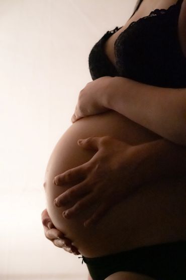Pregnant woman gently cradling her belly in soft lighting.