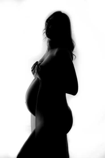 Silhouette of a pregnant woman softly holding her belly and chest.