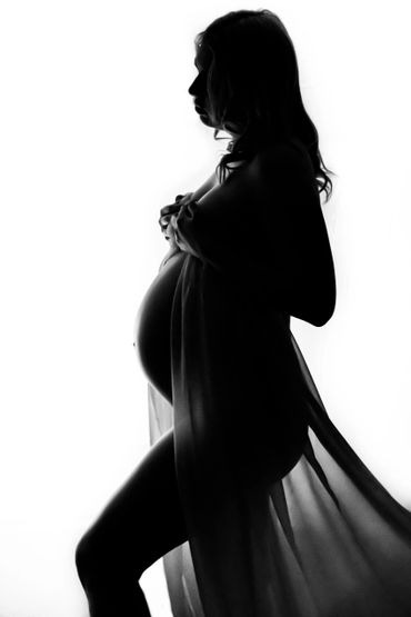 Silhouette of a pregnant woman holding a sheer fabric.