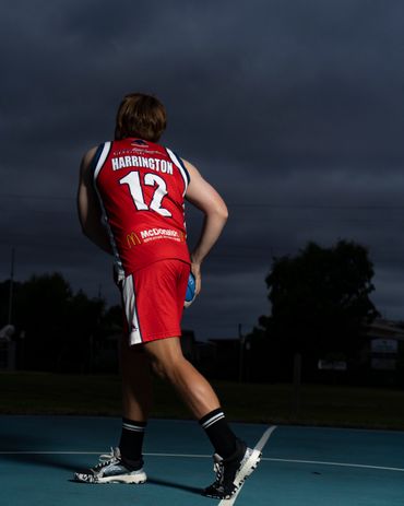 Basketball player Harrington in red uniform prepares to dribble on an outdoor court at dusk.
