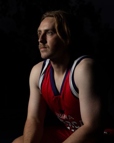 A man in a red sports jersey gazes thoughtfully into the distance against a dark background.