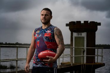 Athlete holding a football by a lakeside structure under a cloudy sky.