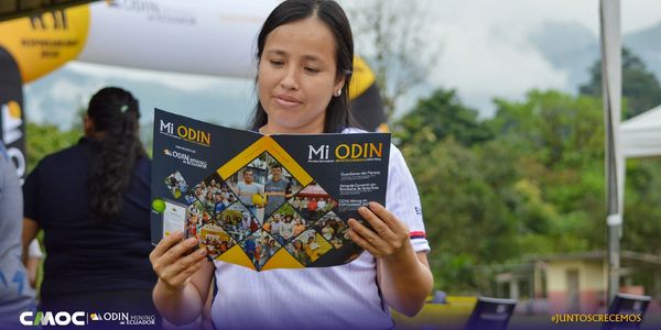 A woman reads a brochure titled 'Mi ODIN' outdoors at an event.