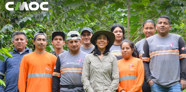 Group of people posing outdoors in nature, some wearing orange and gray shirts with logos.