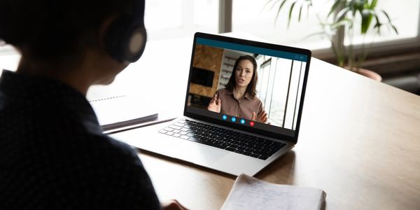 Person attending a video call on a laptop while taking notes.