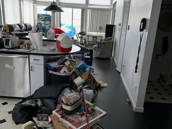 Messy kitchen and living area with clutter on the floor and countertop.