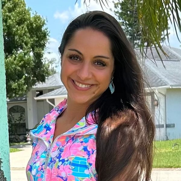 Smiling woman with long hair in a colorful floral jacket outdoors.