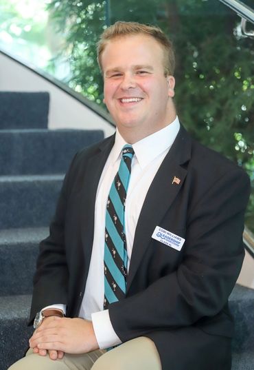 Young man in business attire smiling indoors on a staircase.