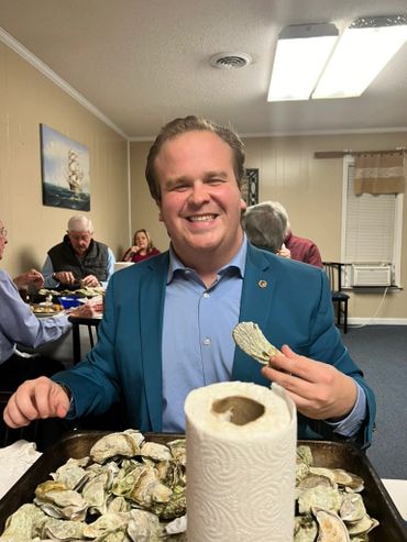 Smiling man in blue jacket enjoying fresh oysters at a casual gathering.