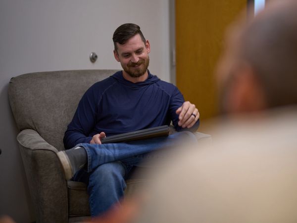 Man in casual clothes sitting comfortably on a chair, holding a tablet, smiling.