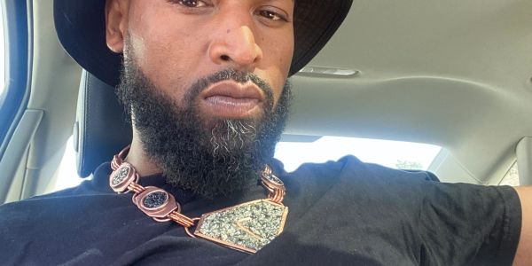 Man with beard wearing a black hat and necklace.