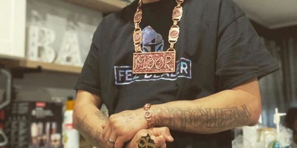 Person wearing jewelry and a black t-shirt with tattoos on arms.