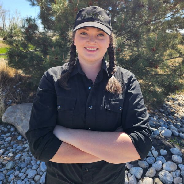 Woman in black shirt and cap stands outdoors with arms crossed, smiling.