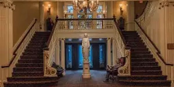 Elegant grand staircase with chandelier and statue in a classic interior.