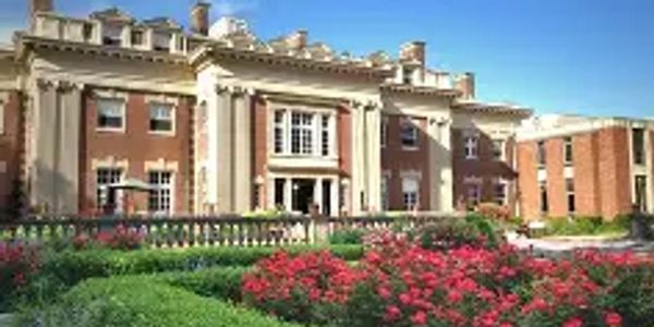 Historic mansion with a beautiful garden under a clear blue sky.