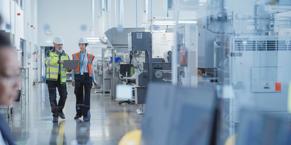 Two engineers walking in a factory with a laptop.