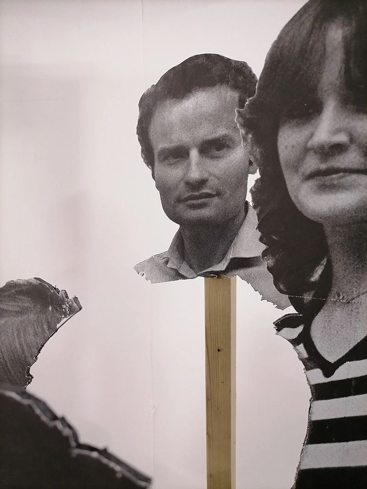 Black and white cutouts of faces mounted on sticks against a plain background.