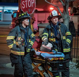 Two white firefighters standing by, next to a stretcher at a fire.