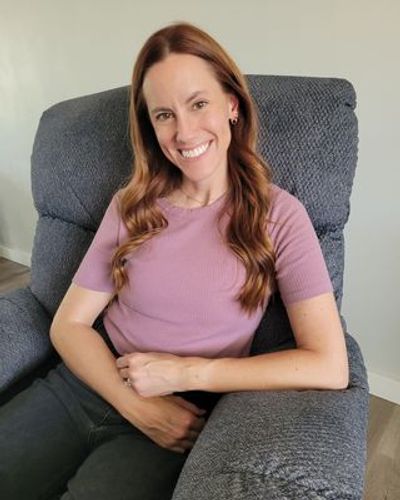 A smiling woman with long hair sitting on a gray armchair.