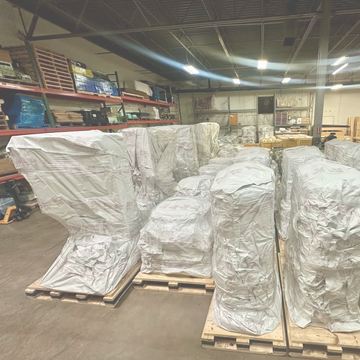 Large industrial items covered in protective plastic on wooden pallets in a warehouse.