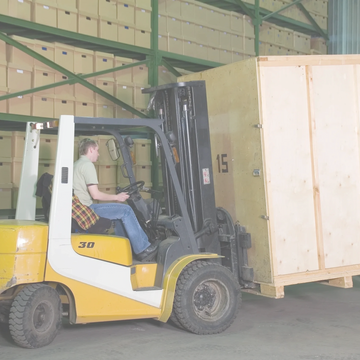 Warehouse worker operating a forklift to move a large wooden crate.