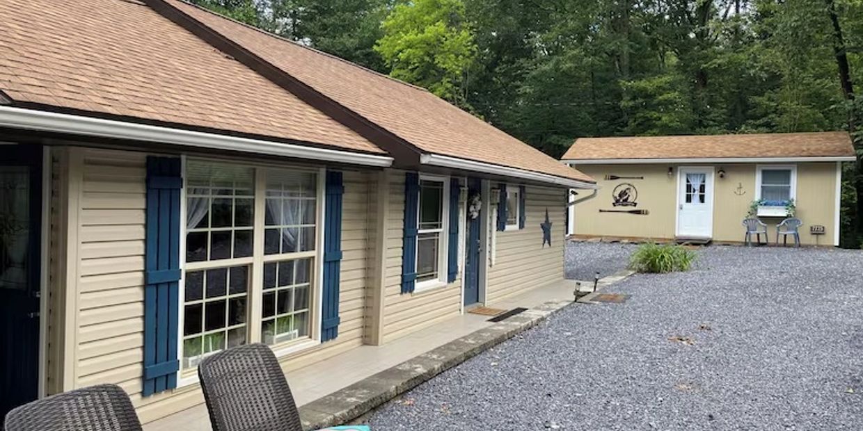 Beige house with blue shutters and a gravel driveway.