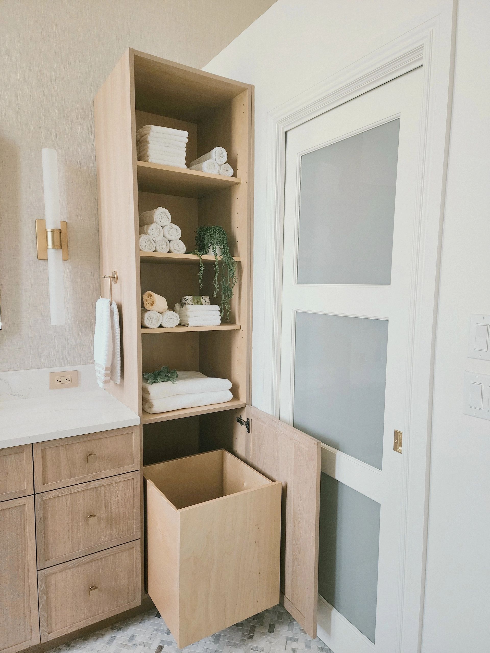 Bathroom cabinet with neatly arranged towels and open laundry hamper.