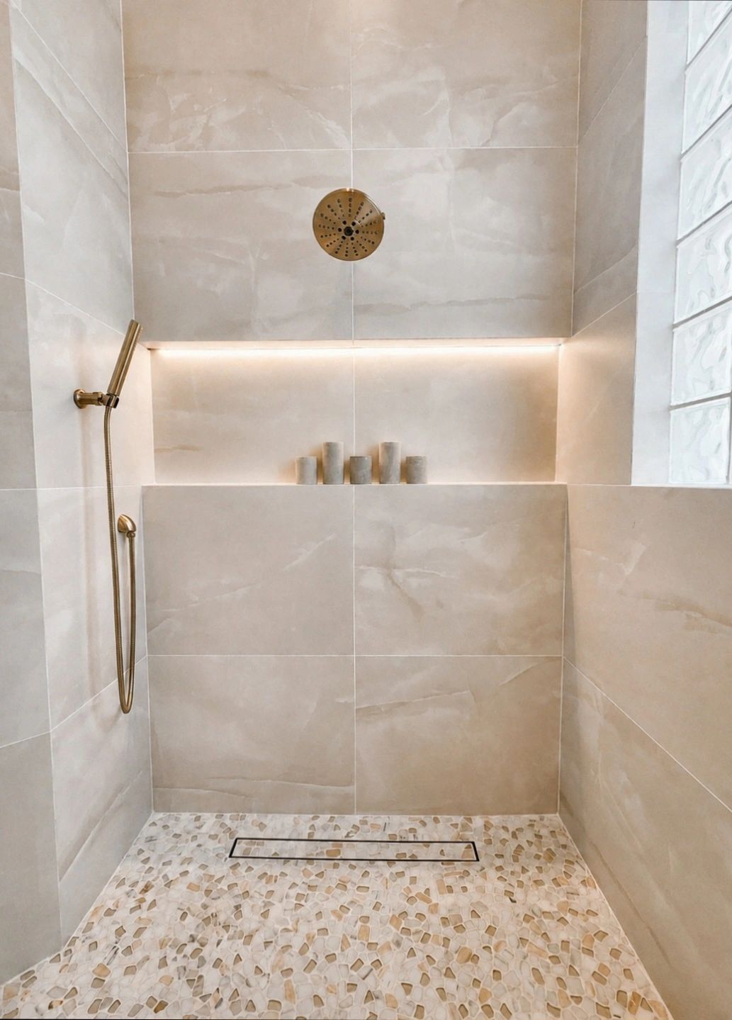 Modern beige tiled shower with pebble flooring and brass fixtures.
