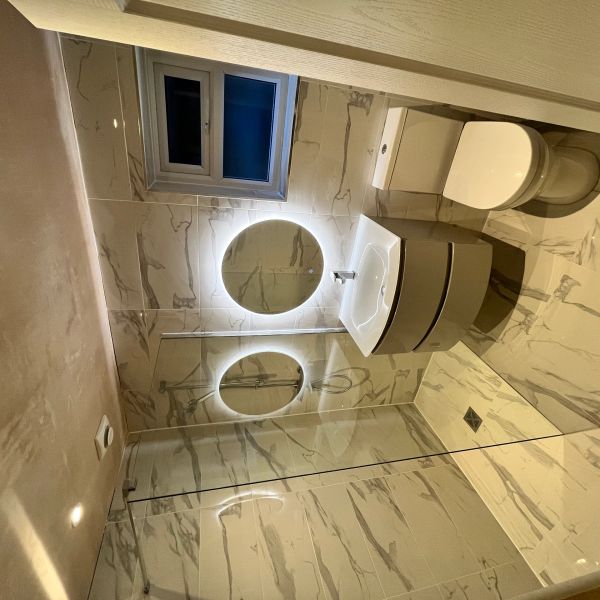 Modern bathroom with illuminated round mirror and walk-in shower.