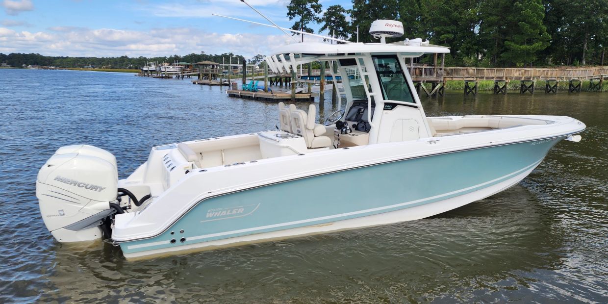 A sleek blue and white Boston Whaler boat on calm water near docks.