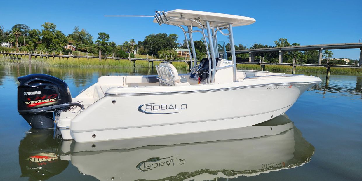 White Robalo boat with Yamaha motor docked on calm water near a bridge.