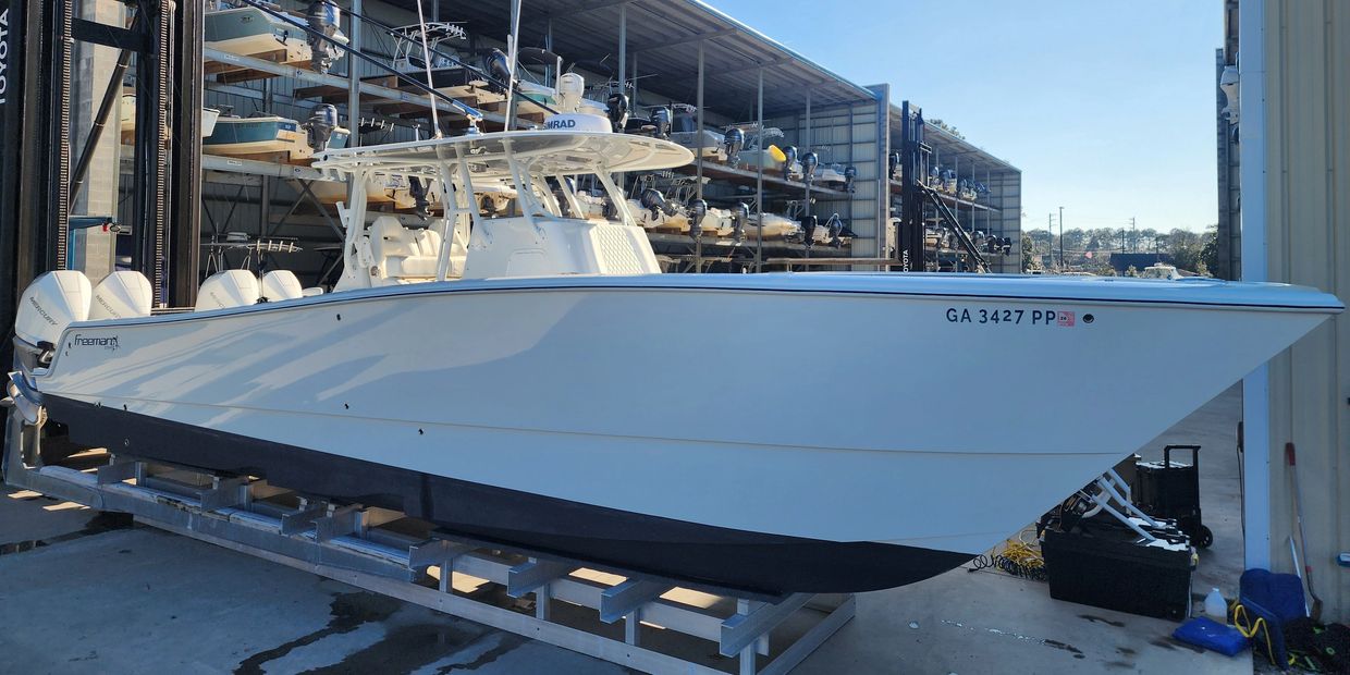 A sleek white fishing boat with triple outboard engines docked at a marina.