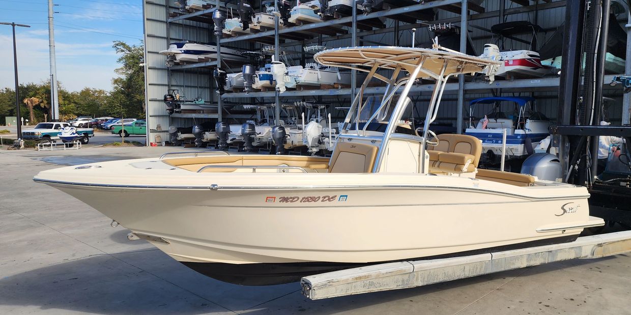A cream-colored center console boat docked on a concrete surface near a boat storage facility.