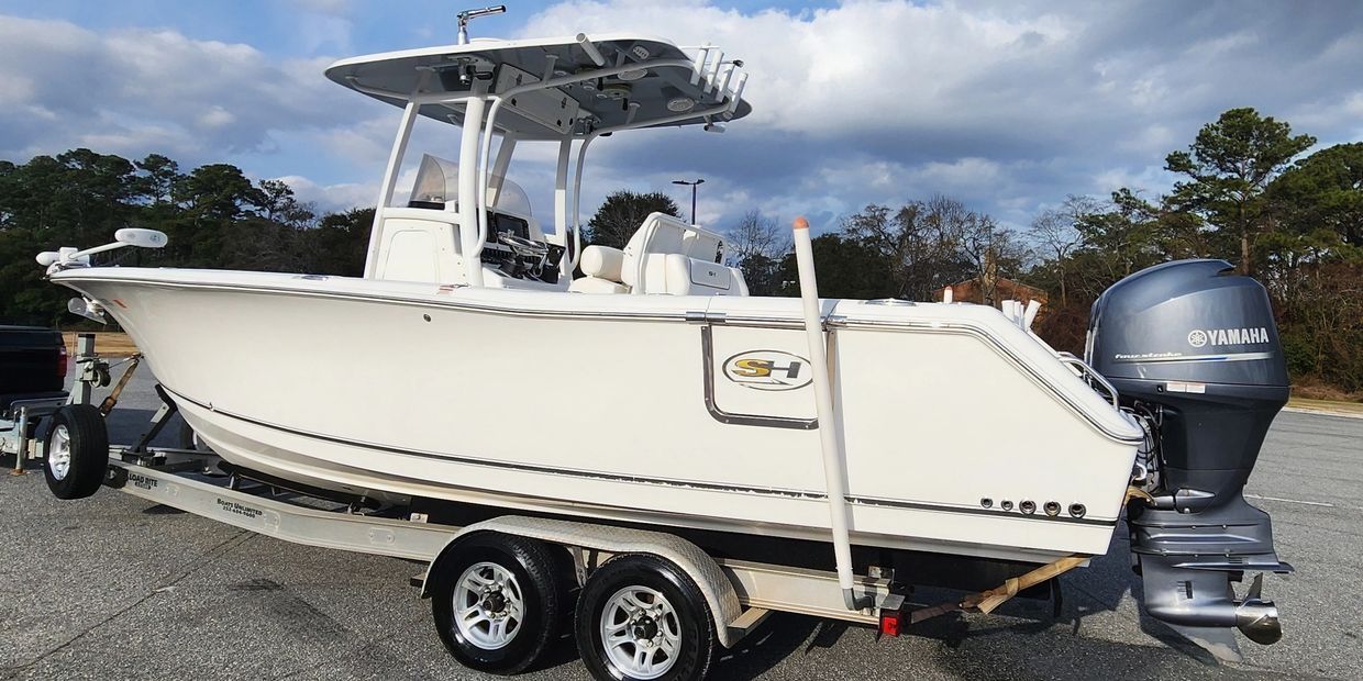 White center console fishing boat on a trailer under a cloudy sky.