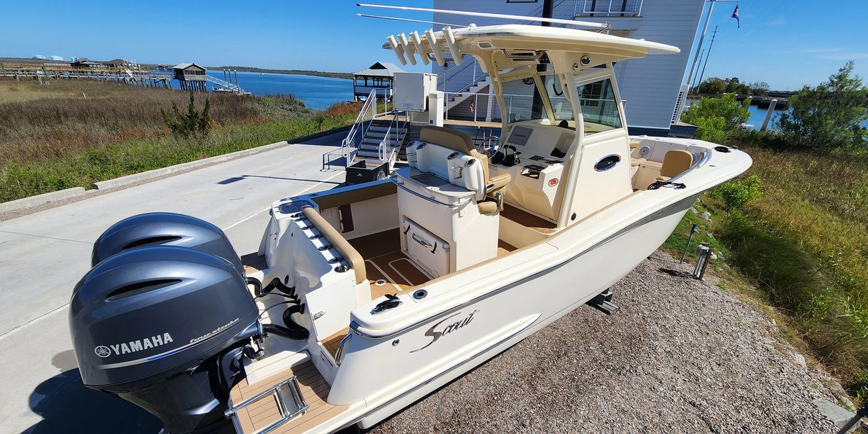 A sleek Scout motorboat with twin Yamaha engines docked near a waterfront house.