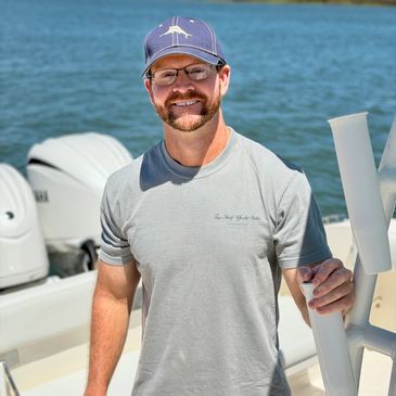 Man in cap smiling on a boat near water.
