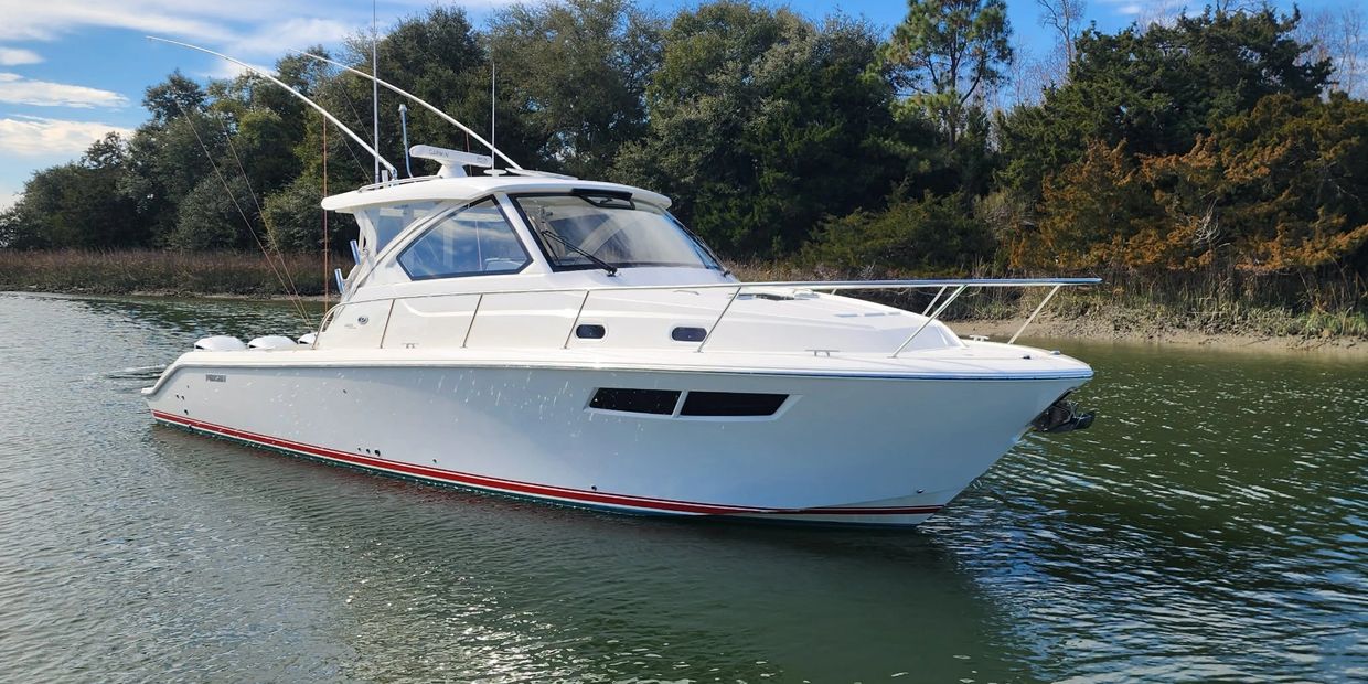 A sleek white fishing boat on calm water near a wooded shore.